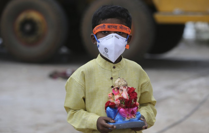 An Indian child wearing a mask as a precaution against the coronavirus carries an idol of elephant-headed Hindu god Ganesha to immerse in Saroornagar Lake on the final day of Ganesh Chaturthi