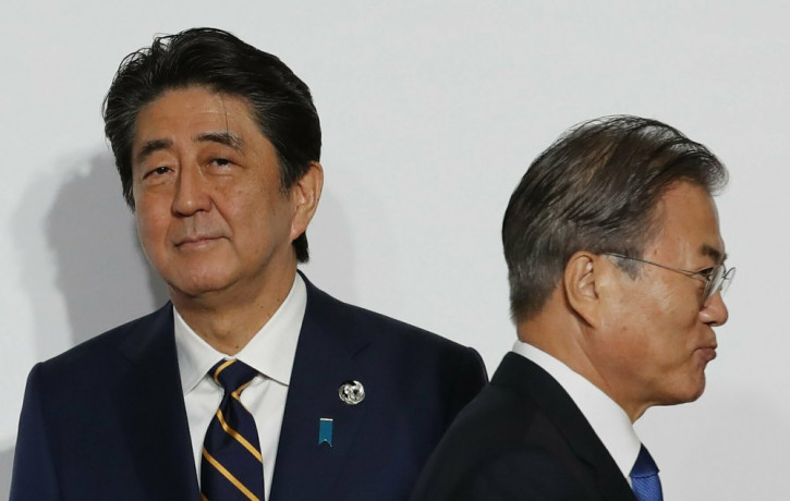 In this June 28, 2019, file photo, South Korean President Moon Jae-in, right, walks by Japanese Prime Minister Shinzo Abe upon his arrival for a welcome and family photo session at the G-20 l
