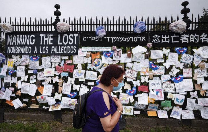 In this May 28, 2020, file photo, a woman passes a fence outside Brooklyn's Green-Wood Cemetery adorned with tributes to victims of COVID-19 in New York.