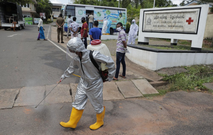 A Sri Lankan health worker sprays disinfectants as people wait to give swab samples to test for COVID-19 near a mobile testing vehicle outside a hospital in Minuwangoda, Sri Lanka, Tuesday, O