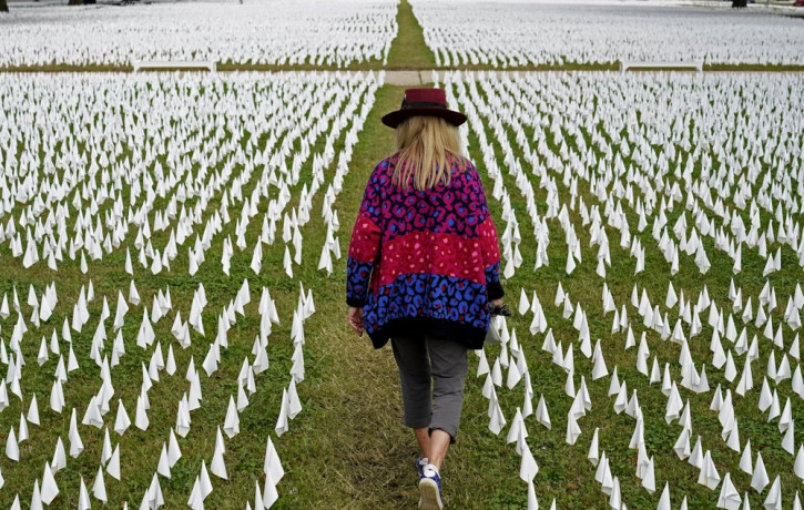 In this Oct. 27, 2020, Artist Suzanne Brennan Firstenberg walks among thousands of white flags planted in remembrance of Americans who have died of COVID-19 near Robert F. Kennedy Memorial St