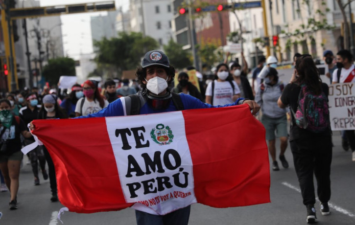 A supporter of ousted President Martin Vizcarra holds a banner with a message that reads in Spanish, "I love you Peru, how could I not," as people refusing to recognize the new government mar