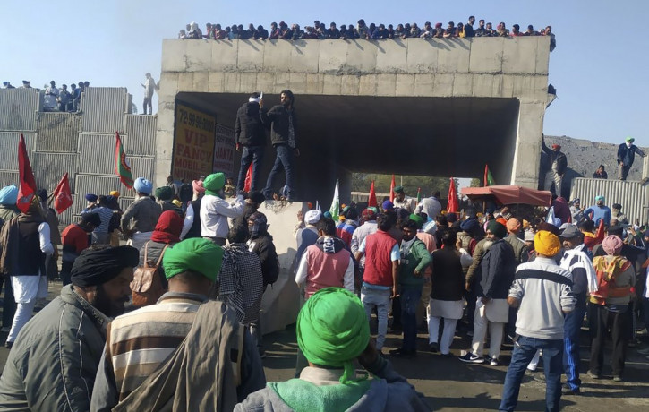 Farmers stand on an under construction flyover and watch attempts of concrete barricades being removed by fellow farmers, set up by security officers to prevent their protest march to Delhi, 