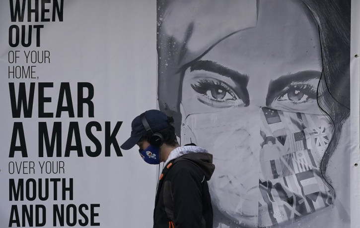 In this Nov. 21, 2020, file photo, a pedestrian walks past a mural reading: "When out of your home, Wear a mask over your mouth and nose," during the coronavirus outbreak in San Francisco.