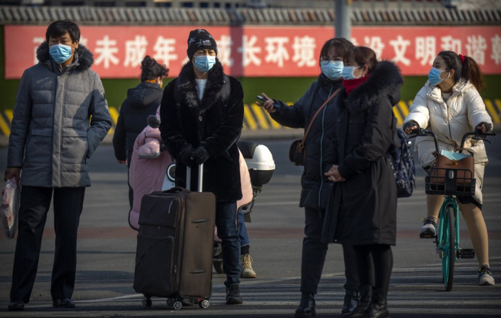 People wearing face masks to protect against the spread of the coronavirus wait to cross an intersection in Beijing, Wednesday, Jan. 20, 2021.