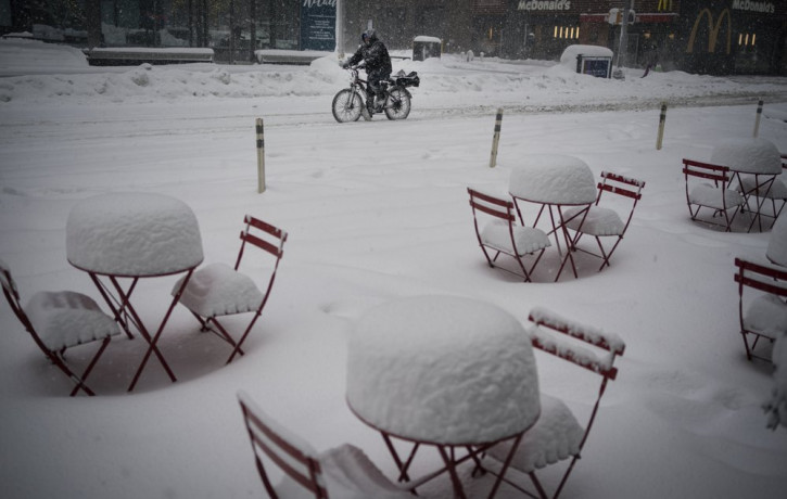 A man delivers food on his electric bicycle as he rides past snow-covered dining tables in midtown during a snowstorm, Monday, Feb. 1, 2021, in New York.