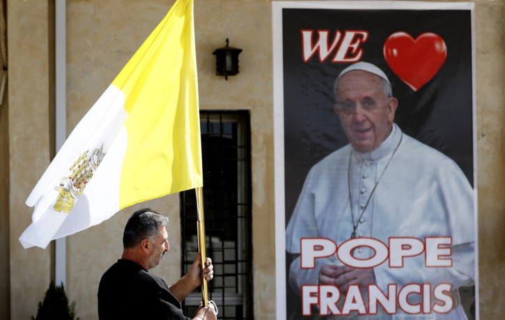 A Christian priest holds a Vatican flag as he walks by a poster of Pope Francis during preparations for the Pope's visit in Mar Youssif Church in Baghdad, Iraq, Friday, Feb. 26, 2021.