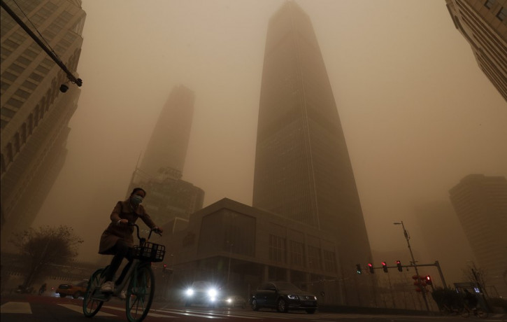 A cyclist and motorists move past office buildings amid a sandstorm during the morning rush hour in the central business district in Beijing, Monday, March 15, 2021.