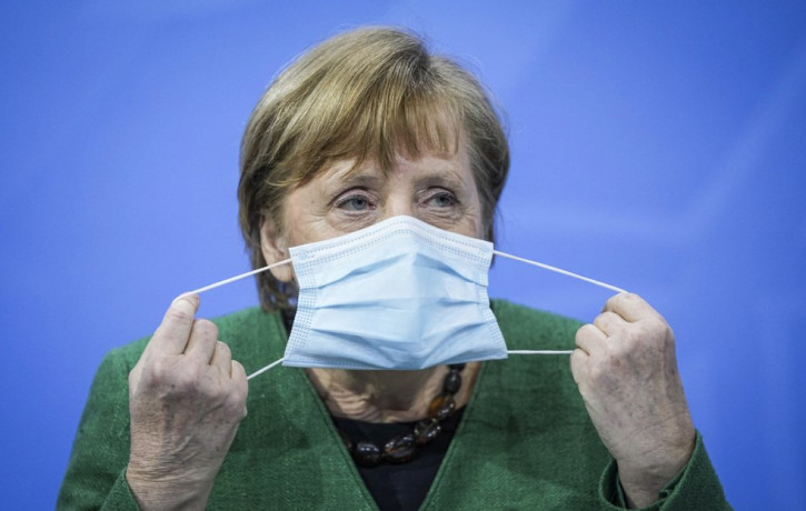 German Chancellor Angela Merkel removes her mask at the start of a press conference in the Chancellor's Office following consultations between the federal and state governments in Berlin Tues