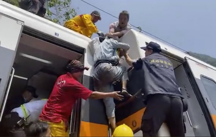 In this image made from a video released by hsnews.com.tw, a passenger, center, is helped to climb out of a derailed train in Hualien County in eastern Taiwan Friday, April 2, 2021.
