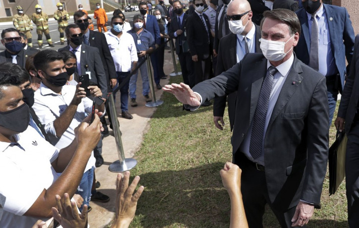 Wearing a mask to curb the spread of the new coronavirus, Brazil's President Jair Bolsonaro greets people after a ceremony to deliver affordable homes built by the government, in a neighborho