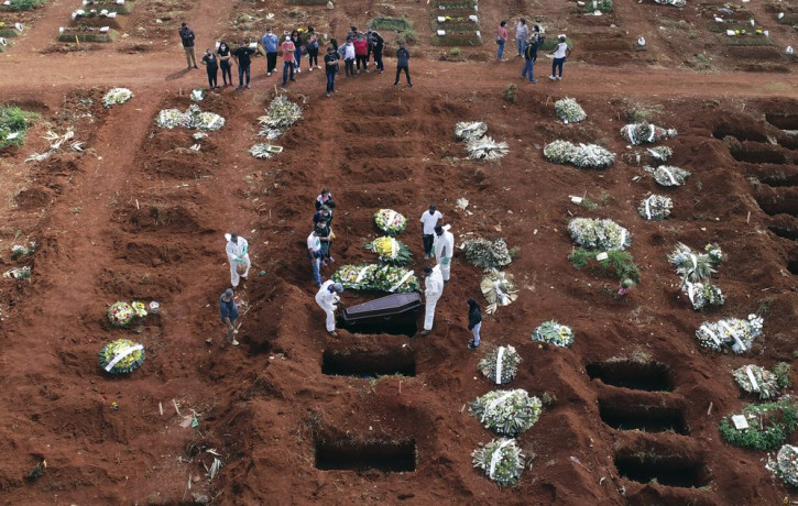 In this April 7, 2021, file photo, cemetery workers wearing protective gear lower the coffin of a person who died from complications related to COVID-19 into a gravesite at the Vila Formosa c