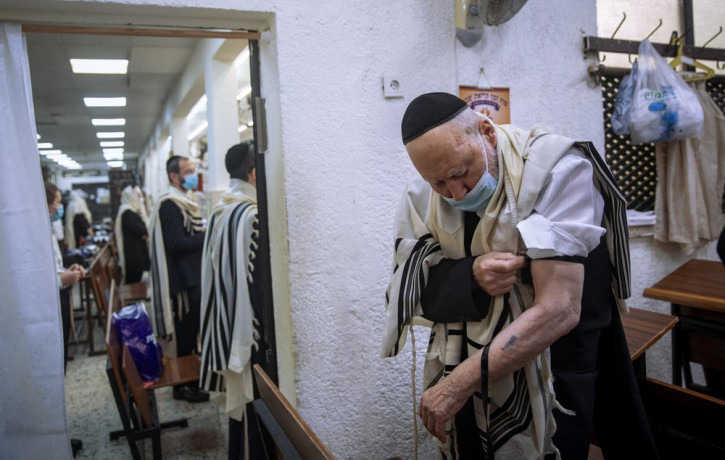 Holocaust survivor Yehoshua Datsinger places tefillin on his arm above the Auschwitz concentration camp identification number tattoo, during morning prayer at a synagogue limited to 20 people