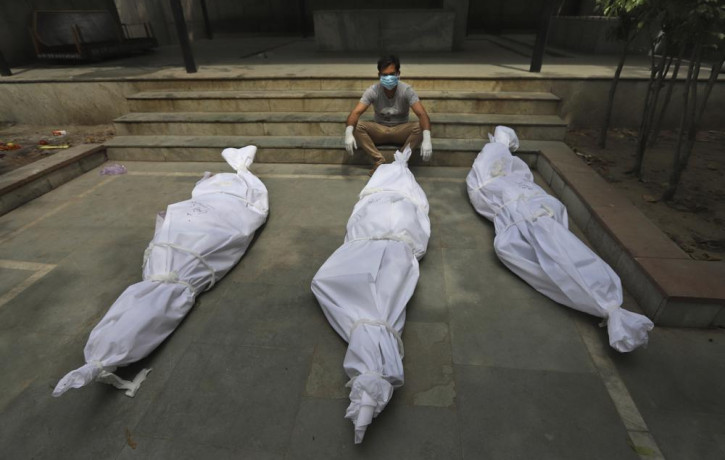 In this April 20, 2021, file photo, a man waits for the cremation of a relative who died of COVID-19, placed near bodies of other victims, in New Delhi, India.