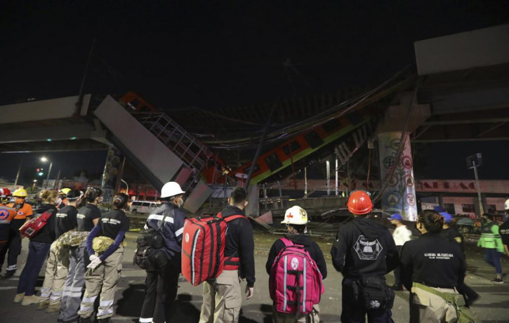 Rescue personnel stand in front of Mexico City subway cars laying at an angle after a section of Line 12 of the subway collapsed in Mexico City, Tuesday, May 4, 2021.