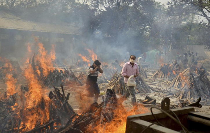 In this April 29, 2021, file photo, relatives react to heat emitting from the multiple funeral pyres of COVID-19 victims at a crematorium in the outskirts of New Delhi, India.