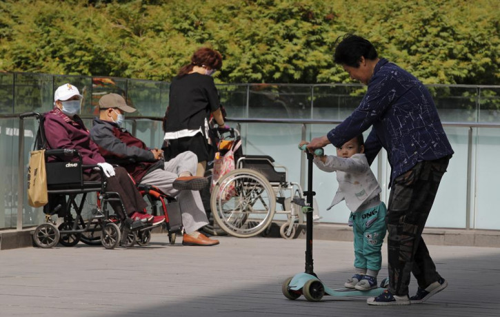 A woman plays with a child near elderly people on wheelchairs sunbathing on a compound of a commercial office building in Beijing on Monday, May 10, 2021.
