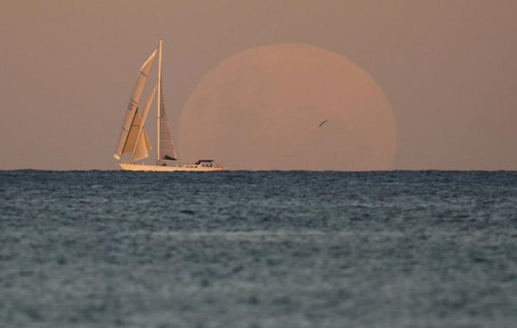 A yacht sails past as the moon rises in Sydney Wednesday, May 26, 2021.