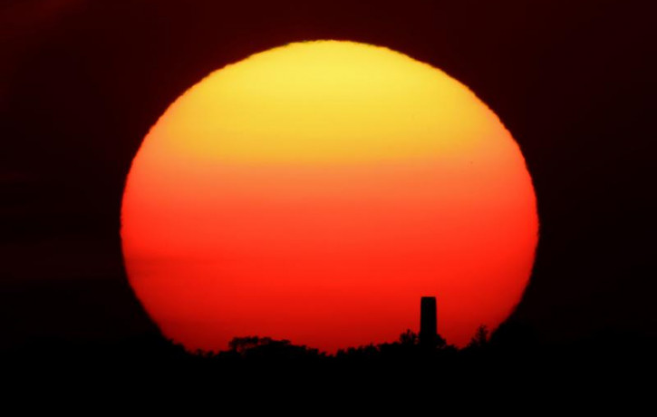 In this Friday, June 26, 2020 file photo, the sun sets behind a smokestack in the distance in Kansas City, Missouri.