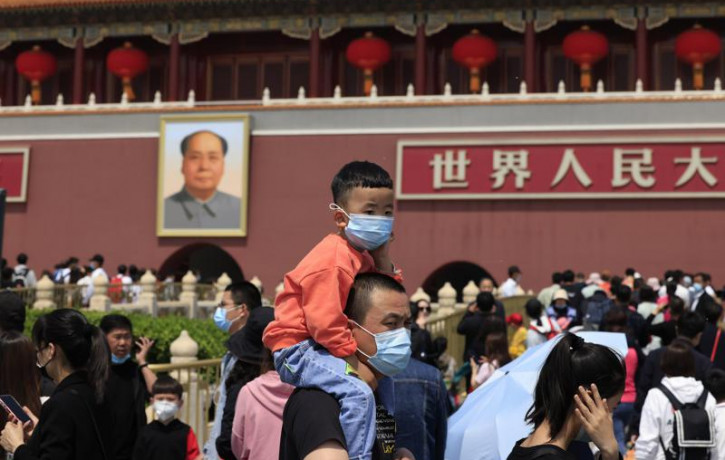 In this May 3, 2021, file photo, a man and child wearing masks visit Tiananmen Gate near the portrait of Mao Zedong in Beijing.