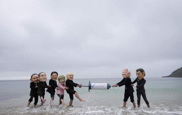 Activists wearing giant heads of the G7 leaders tussle over a giant COVID-19 vaccine syringe during an action of NGO's on Swanpool Beach in Falmouth, Cornwall, England, Friday, June 11, 2021.