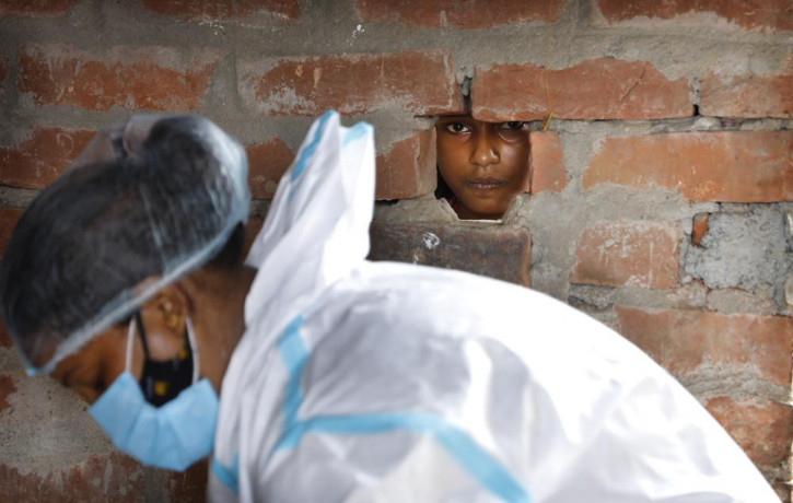 A girl looks out through a hole in the wall of her house as a health worker prepares for COVID-19 testing in Jamsoti village, Uttar Pradesh state, India, on June 9, 2021