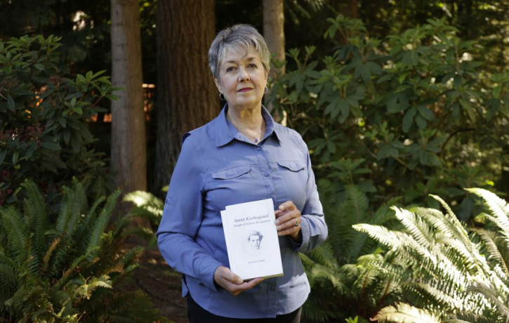 Karen McKnight stands in her backyard on Saturday, June 19, 2021, in Sammamish, Washington, holding two books written by her brother Ross Bagne of Cheyenne, Wyoming.
