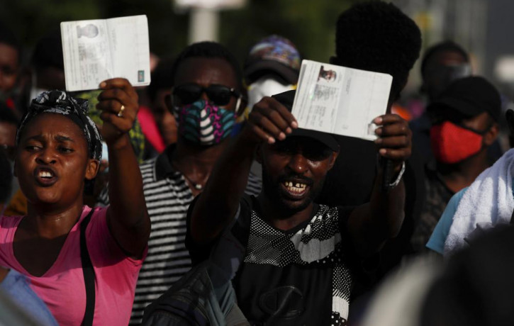 Haitians wave their passports shouting "Help, refugee," as they gather outside the U.S. Embassy in Port-au-Prince, Haiti, Friday, July 9, 2021.