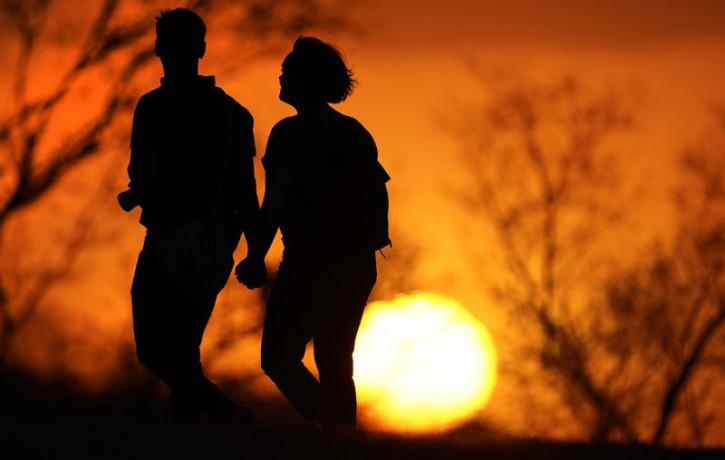 In this Wednesday, March 10, 2021 file photo, a couple walks through a park at sunset in Kansas City, Missouri.