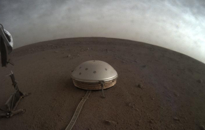 In this undated photo made available by NASA on Thursday, July 22, 2021, clouds drift over the dome-covered SEIS seismometer of the InSight lander on the surface of Mars.