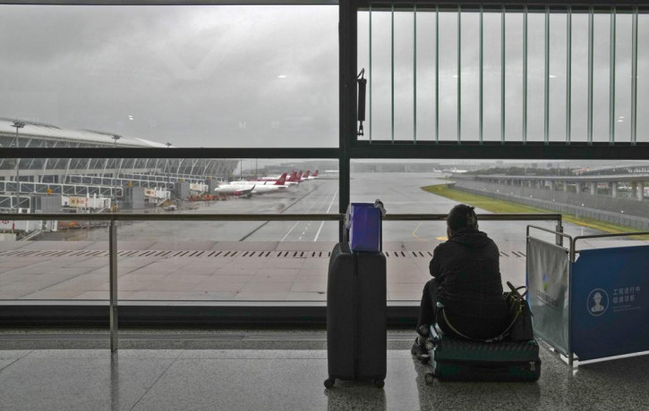 A passenger sits on her luggage watching passenger airplanes parked on the tarmac after all flights were canceled at Pudong International Airport in Shanghai, China, Sunday, July 25, 2021.