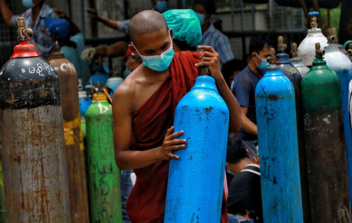 In this July 28, 2021, file photo, Buddhist monk wearing a face mask holds an oxygen tank for refill outside the Naing oxygen factory at the South Dagon industrial zone in Yangon, Myanmar.