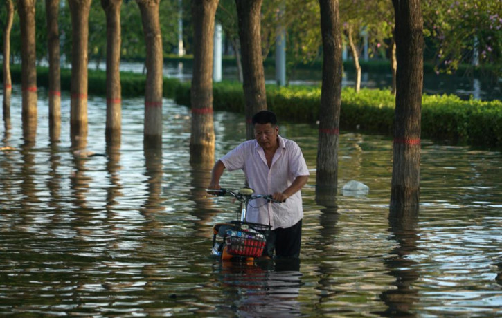 In this July 26, 2021, file photo, a man pushes a scooter through floodwaters in Xinxiang in central China's Henan Province, Monday, July 26, 2021.