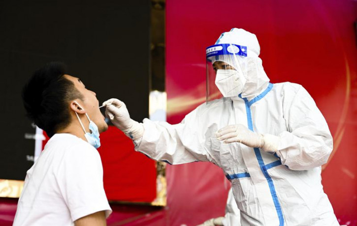 In this July 5, 2021, file photo released by Xinhua News Agency, a medical worker collects a swab sample for nucleic acid test in Ruili City of southwest China's Yunnan Province.