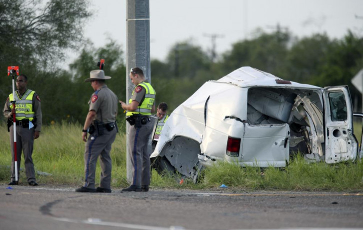 Texas Department of Public Safety officers stand near a vehicle where multiple people died after the van carrying migrants tipped over just south of the Brooks County community of Encino on W
