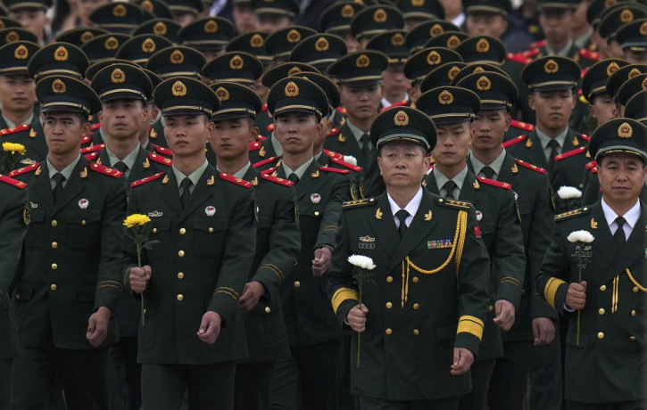 Paramilitary policemen and military officers hold flowers walk to pay respects to the People's Heroes Monument during a ceremony to mark Martyr's Day at Tiananmen Square in Beijing, Thursday,