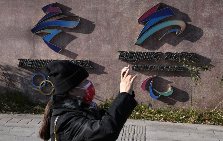 A woman wearing takes photos near the logos for the Beijing Winter Olympics and Paralympics in Beijing, China, Tuesday, Nov. 9, 2021.