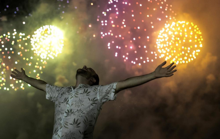 A man celebrates the start of the New Year, backdropped by fireworks exploding in the background over Copacabana Beach in Rio de Janeiro, Brazil, Saturday, Jan. 1, 2022.