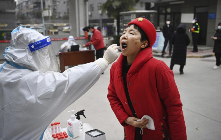 In this photo released by China's Xinhua News Agency, a worker wearing protective gear gives a COVID-19 test to a woman at a testing site in Xi'an in northwestern China's Shaanxi Province, Tu