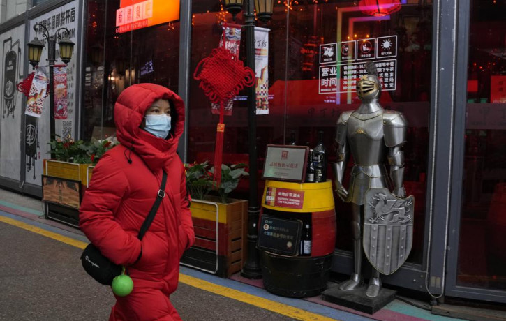 A woman wearing a mask to protect from the coronavirus walks past a coat of armour displayed outside a restaurant in Beijing, China, Friday, Jan. 21, 2022.