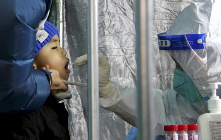 In this photo released by Xinhua News Agency, a child gets a throat swab for the COVID-19 test at a residential area in Fengtai District in Beijing, Sunday, Jan. 23, 2022.