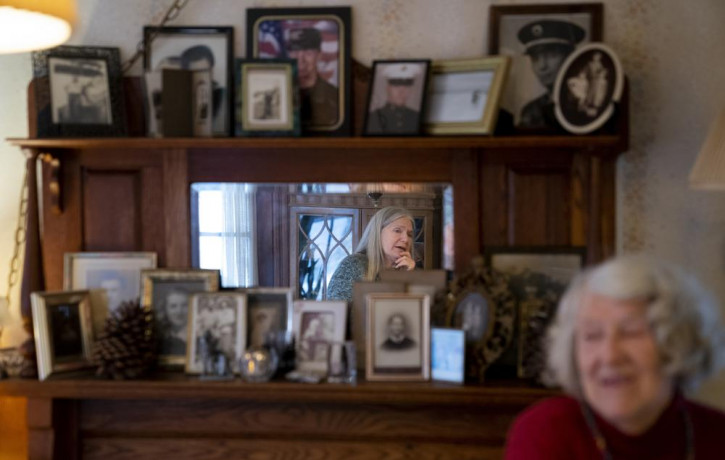 Nancy Rose, center in mirror, speaks with her mother, Amy Russell, right, who both contracted COVID-19 in 2021, in their dining room surrounded by pictures of relatives and family, Tuesday, J