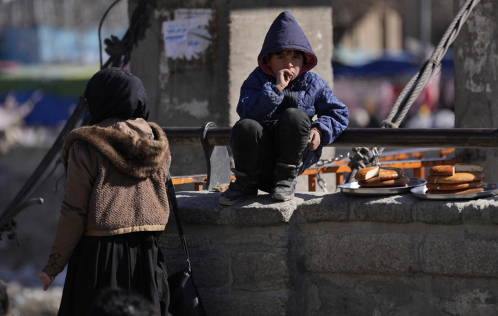 A boy selling bread watches Muslims attending Friday Prayer in Kabul, Afghanistan, Friday, Feb. 11, 2022.