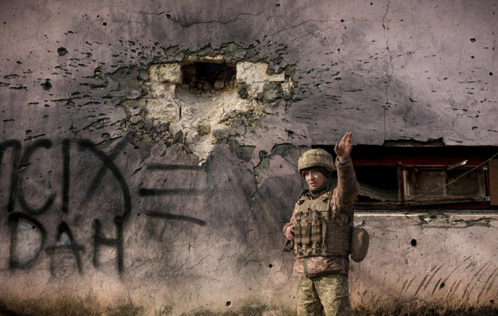 A Ukrainian serviceman points to the direction of the incoming shelling next to a building which was hit by a large caliber mortar shell in the frontline village of Krymske, Luhansk region, i