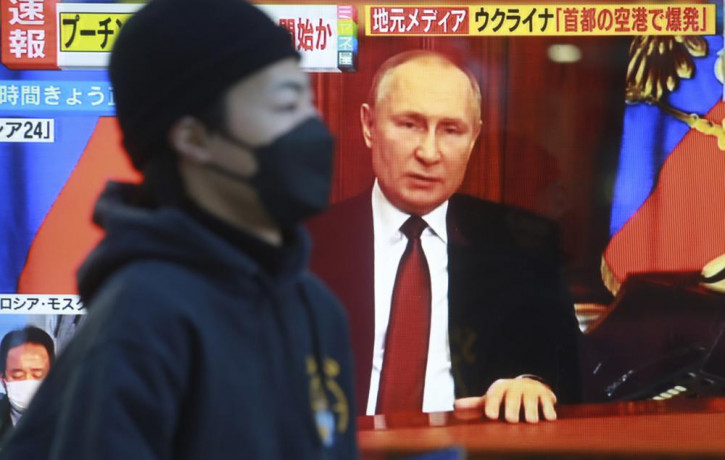 A man walks past a TV screen with image of Russia's President Vladimir Putin in Tokyo, Thursday, Feb. 24, 2022.
