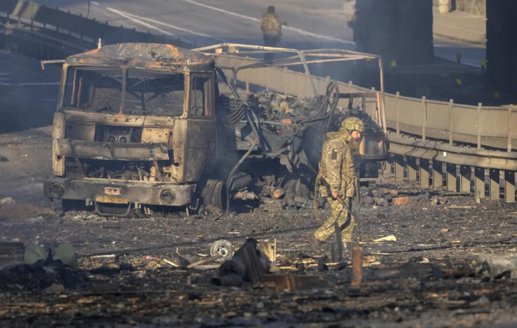 A Ukrainian soldier walks past debris of a burning military truck, on a street in Kyiv, Ukraine, Saturday, Feb. 26, 2022.