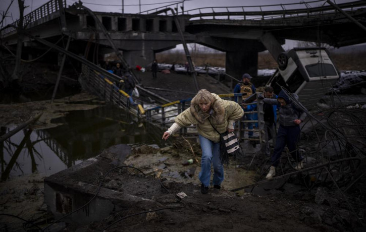 A woman runs as she flees with her family across a destroyed bridge in the outskirts of Kyiv, Ukraine, Wednesday, March 2. 2022.