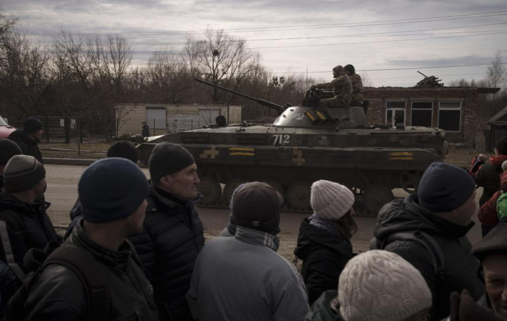 Residents lining up for aid watch as Ukrainian soldiers ride atop a tank in the town of Trostsyanets, Ukraine, Monday, March 28, 2022.