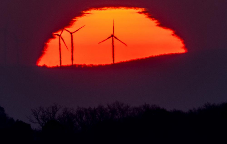 Wind turbines stand in front of the rising sun in Frankfurt, Germany, Friday, March 11, 2022.