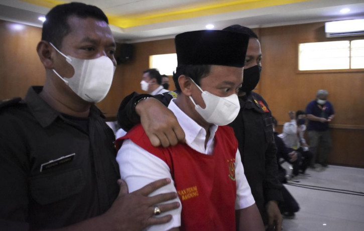 Herry Wirawan, center, the principal of a girls Islamic boarding school accused of raping his students, is escorted by security officers upon arrival for his sentencing hearing at a district 